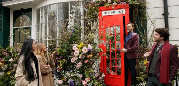 A London street featuring a red telephone box with an abundance of flowers spilling out of it.