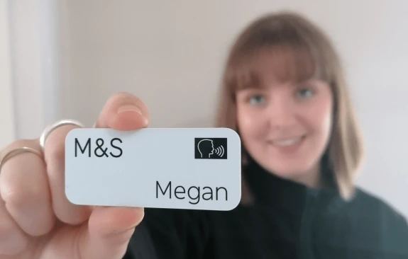 Woman holding M&S name badge with symbol indicating she stammers.