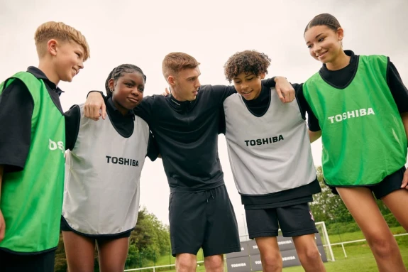 Image of footballer Cole Palmer standing with a group of children in Toshiba T-shirts.