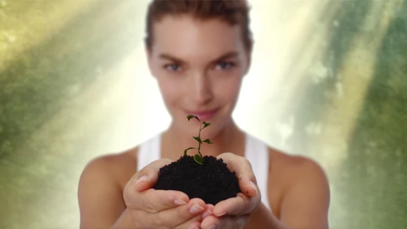 Model Arizona Muse holding mound of earth with a seedling sprouting from it.